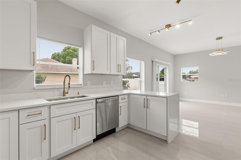 A modern kitchen features white cabinets, quartz countertops, stainless steel appliances, and tile flooring — 1005 CHASE DRIVE, WINTER GARDEN, FL