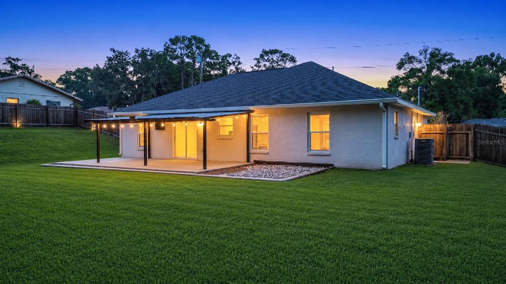 A single-story house with a covered patio, string lights, and a large grassy backyard — 312 CLARK STREET, INVERNESS, FL