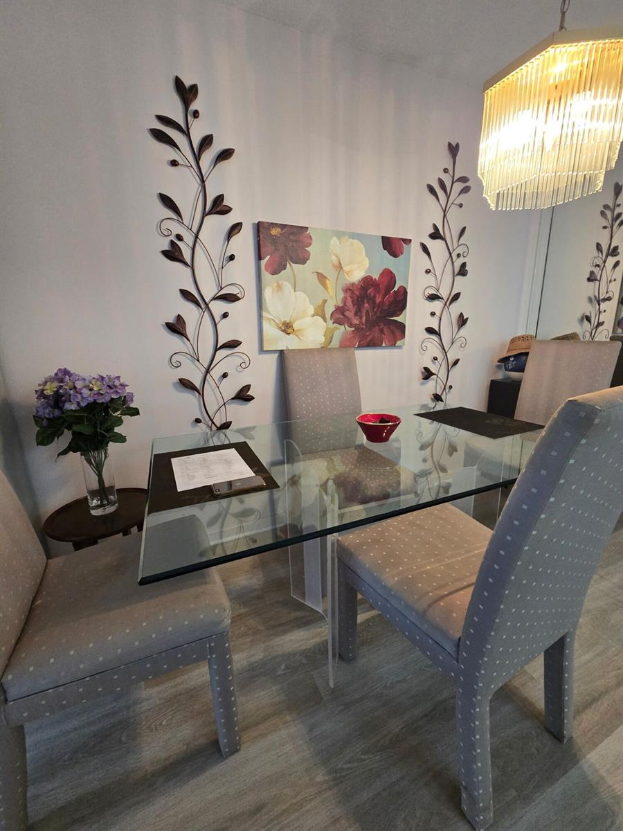 A dining room features a glass-topped table, upholstered chairs, floral wall art, and metal decor — 1010 Berkshire A, Deerfield Beach FL 33442, DEERFIELD BEACH, FL