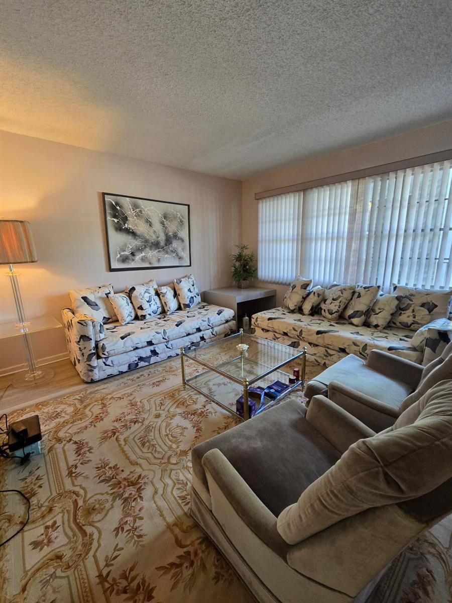 A living room features two patterned sofas, two armchairs, a glass coffee table, and area rug — 1010 Berkshire A, Deerfield Beach FL 33442, DEERFIELD BEACH, FL