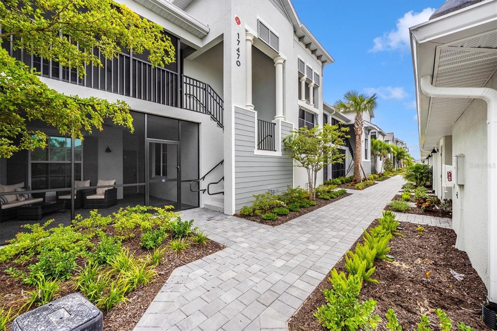 A paved walkway leads past a multi-story apartment building with screened patios and landscaping — 17470 OPAL SAND DRIVE UNIT 205, VENICE, FL