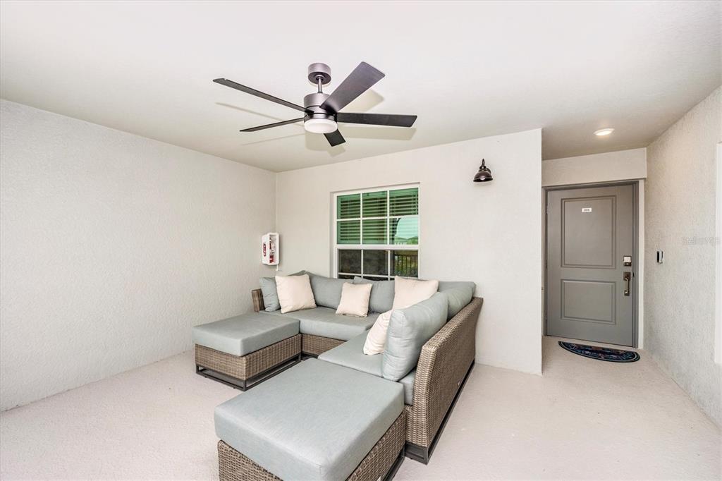 A covered patio features a sectional sofa, a ceiling fan, and a gray entry door — 17470 OPAL SAND DRIVE UNIT 205, VENICE, FL