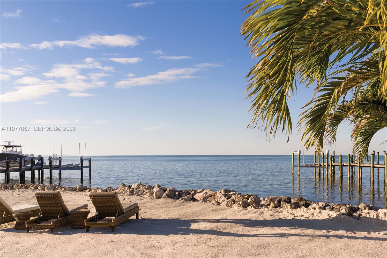 Two lounge chairs sit on a sandy beach overlooking the ocean and wooden docks — 57783 Morton Street, Marathon FL 33050, MARATHON, FL