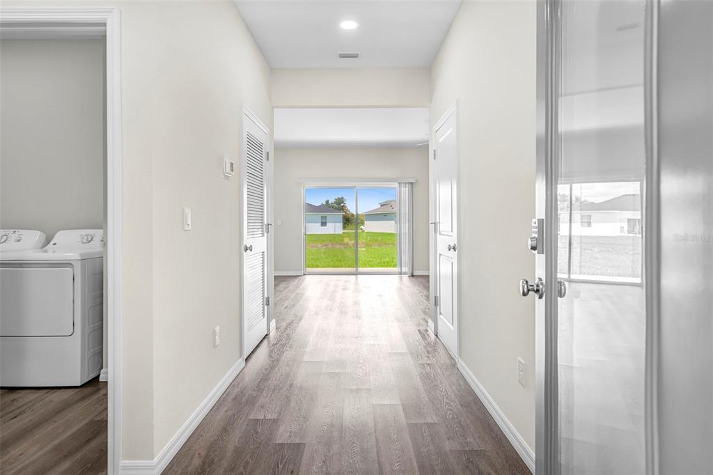A hallway with wood-look flooring leads to a living area with sliding glass doors — 9313 GENTLE BEN COURT, WEEKI WACHEE, FL