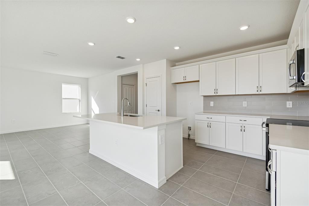A modern kitchen features white cabinets, a central island, and gray tile flooring — 4311 OUTHAUL RUN, PALMETTO, FL
