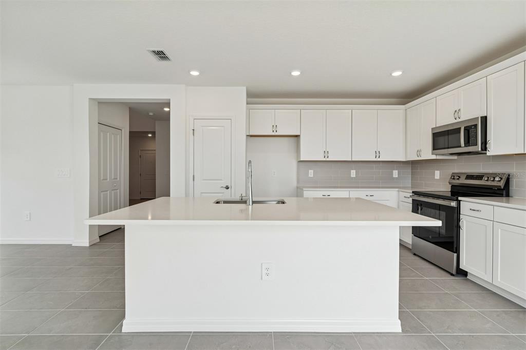 A modern kitchen features white cabinets, a large central island, and stainless steel appliances — 4311 OUTHAUL RUN, PALMETTO, FL