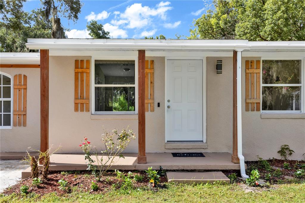 The exterior of a single-story house features a covered porch, white door, and wooden shutters — 247 TOMS ROAD, DEBARY, FL