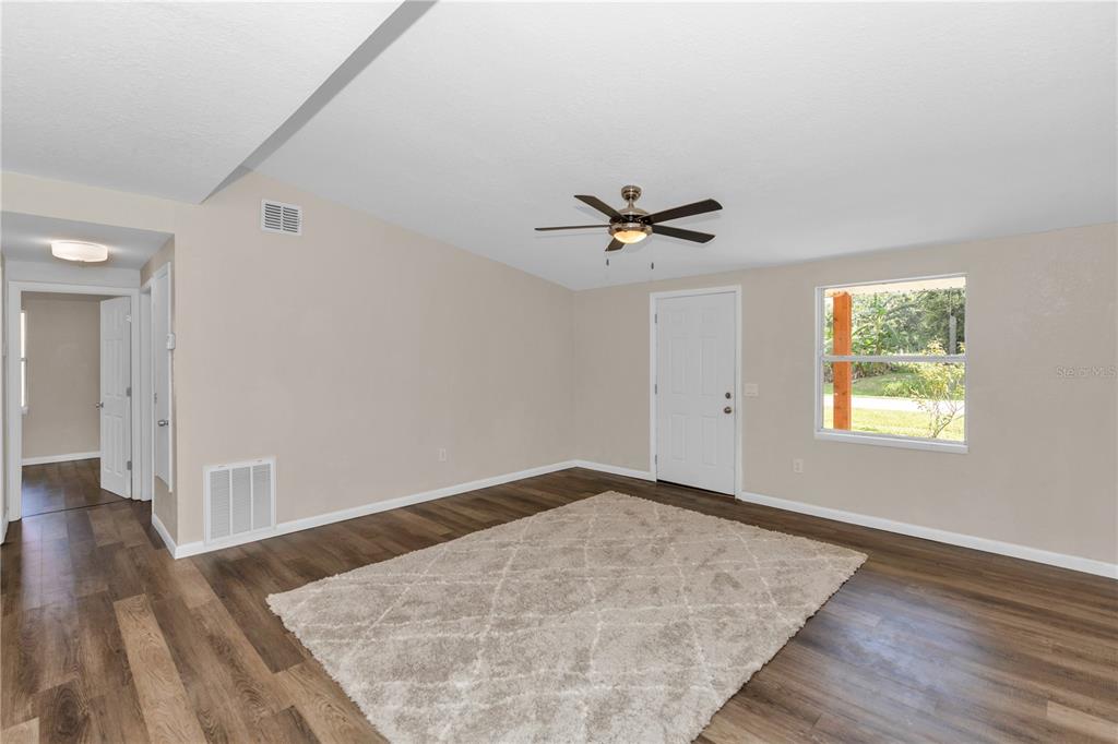 An empty living room features wood-look flooring, a ceiling fan, and a large area rug — 247 TOMS ROAD, DEBARY, FL