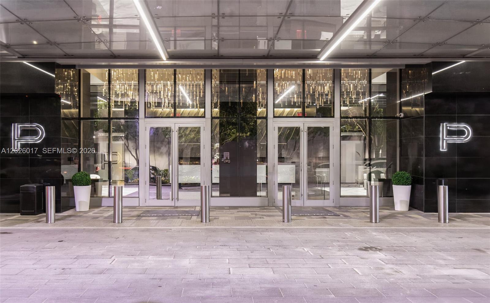 The exterior entrance of a building features glass doors, illuminated P logos, and bollards — 851 NE 1st Ave # 4201, Miami FL 33132, MIAMI, FL