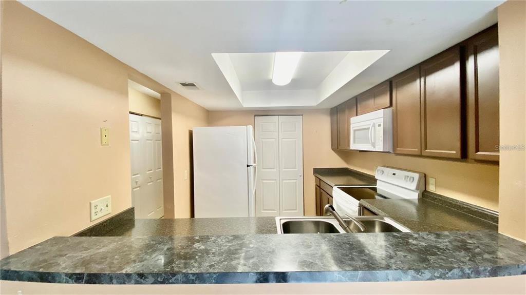 A kitchen features dark wood cabinets, laminate countertops, a white refrigerator, and a breakfast bar — 2528 CITRUS CLUB LANE UNIT 206, ORLANDO, FL