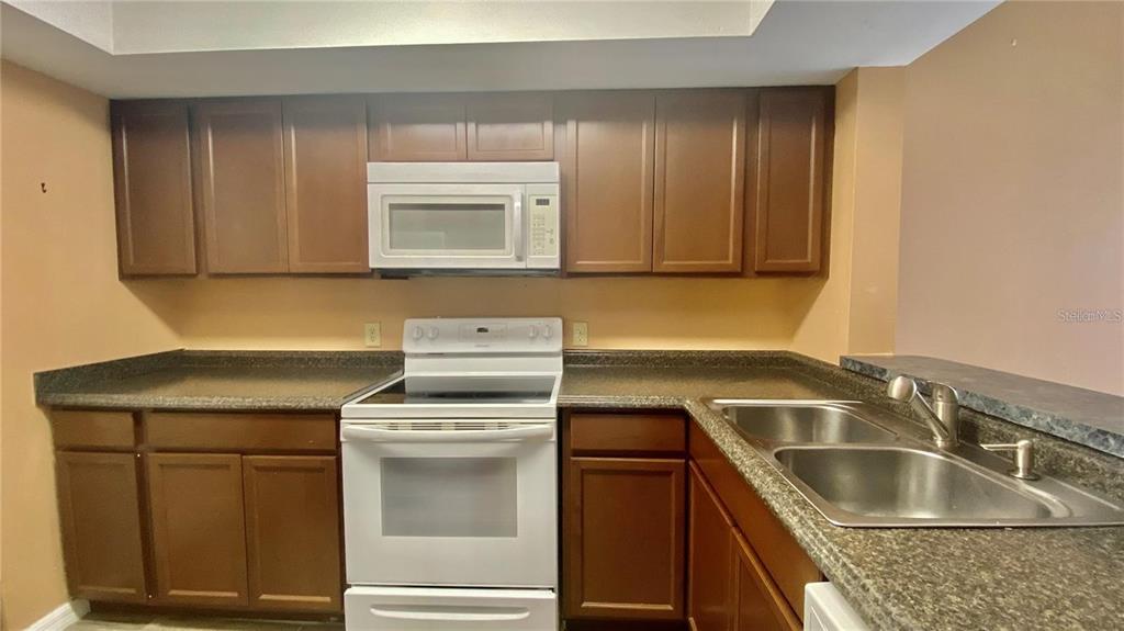 A kitchen features brown wooden cabinets, white appliances, and dark speckled laminate countertops — 2528 CITRUS CLUB LANE UNIT 206, ORLANDO, FL