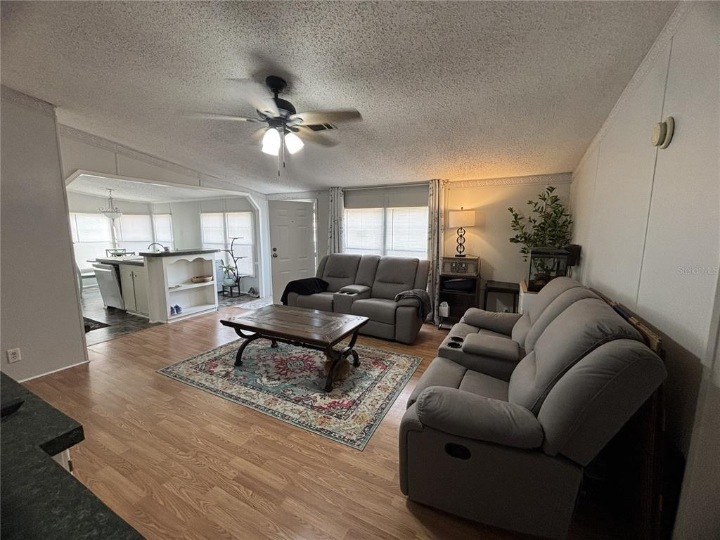 A living room features light wood flooring, two gray reclining sofas, and a ceiling fan — 16564 SE 103RD AVENUE ROAD, SUMMERFIELD, FL