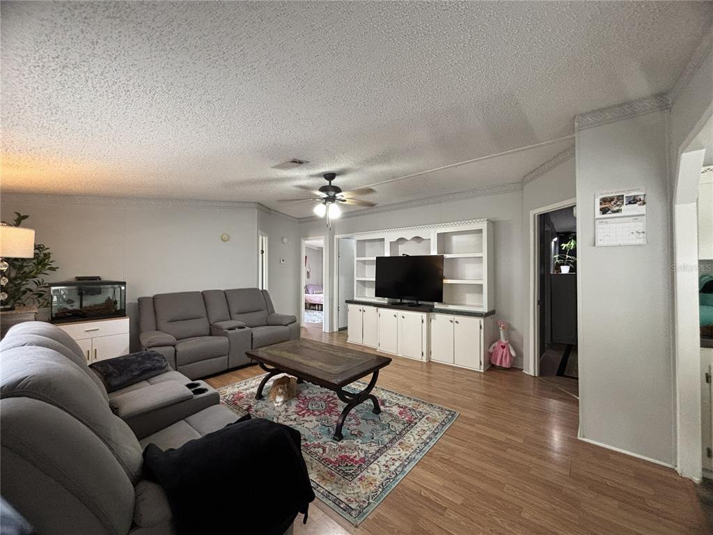A living room features gray reclining sofas, a wooden coffee table, and a built-in entertainment center — 16564 SE 103RD AVENUE ROAD, SUMMERFIELD, FL
