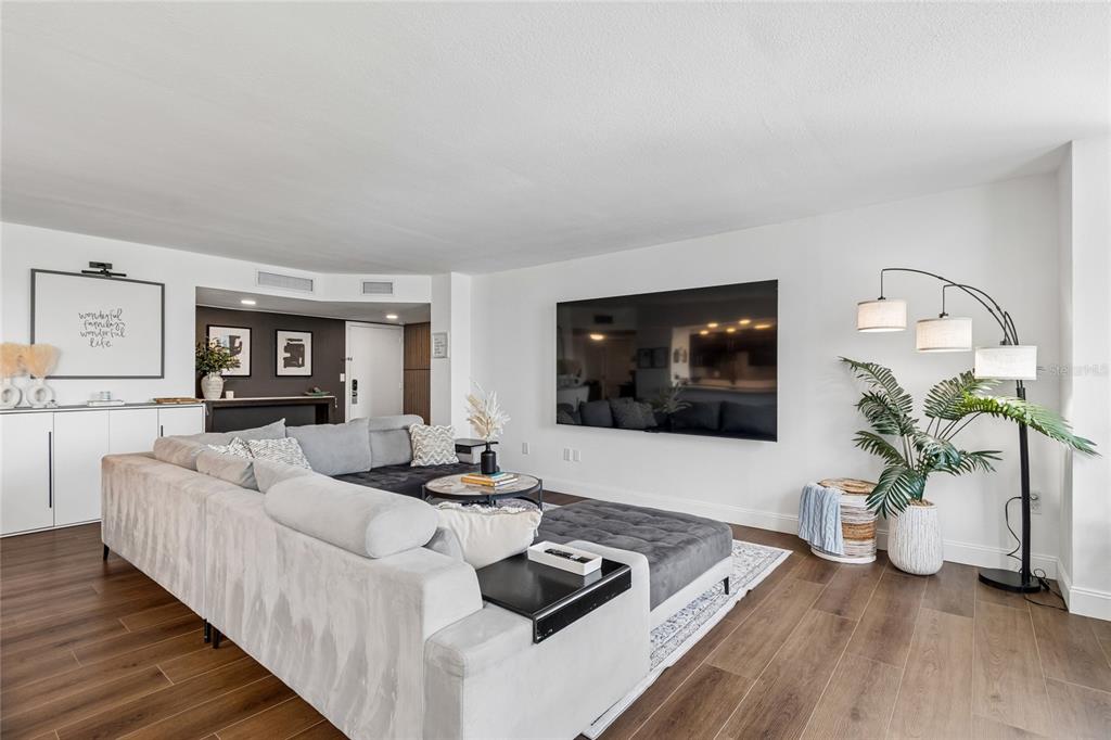 A living room features a large sectional sofa, a wall-mounted television, and wood-look flooring — 644 ISLAND WAY UNIT 405, CLEARWATER, FL
