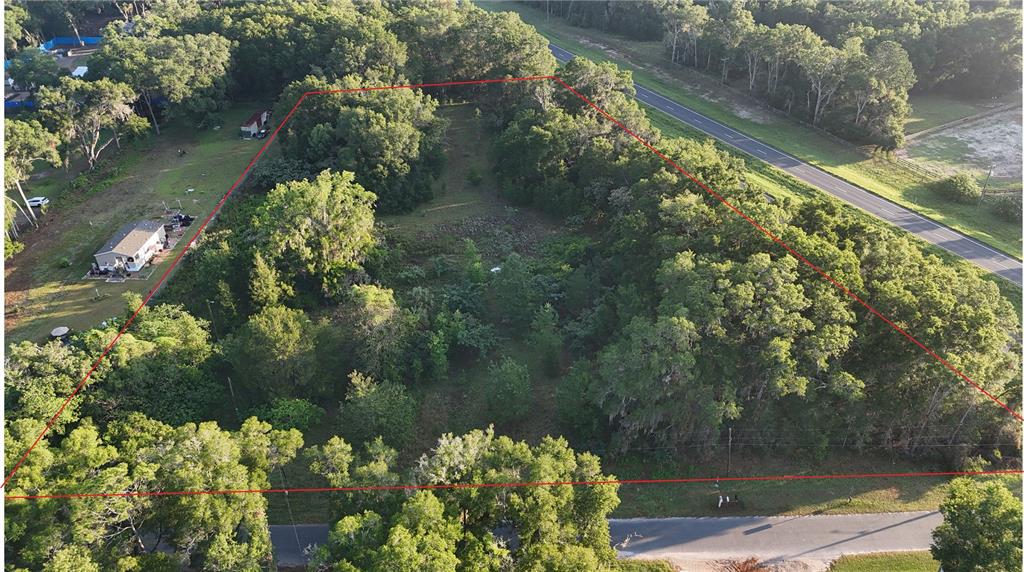 An aerial view shows a wooded, triangular-shaped plot of land bordered by two roads — 2303 NW 145TH STREET, CITRA, FL