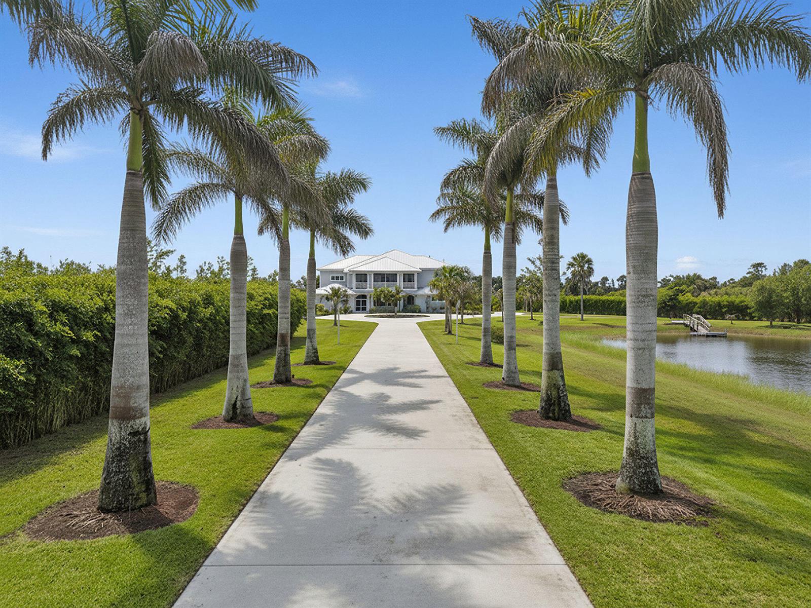 A long concrete driveway lined with palm trees leads to a two-story house — 2985 SW Trailside Path, Stuart FL 34997, STUART, FL