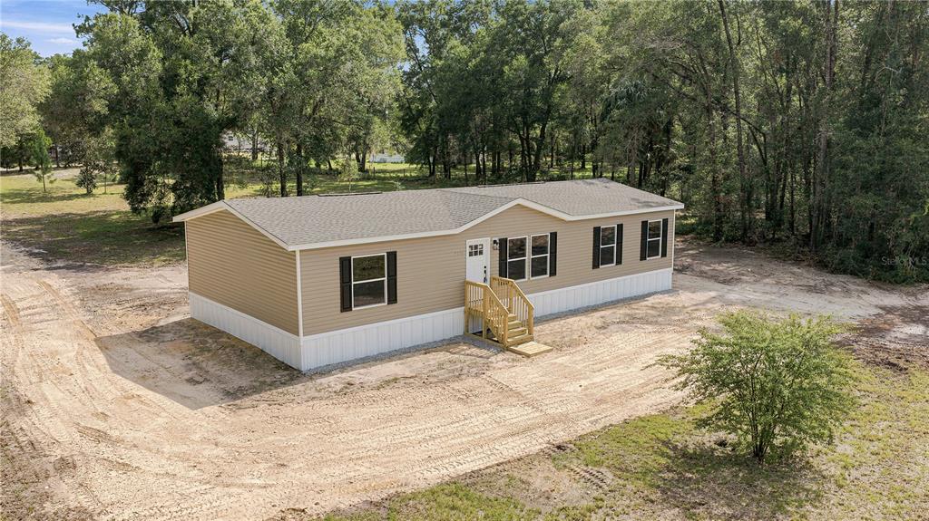 An elevated exterior view of a tan manufactured home with white skirting and wooden steps — 7314 W EDWARDIAN STREET, DUNNELLON, FL