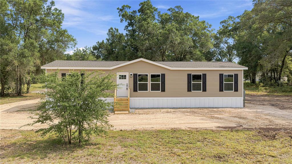 A tan, single-story manufactured home with white skirting sits on a dirt lot with trees — 7314 W EDWARDIAN STREET, DUNNELLON, FL