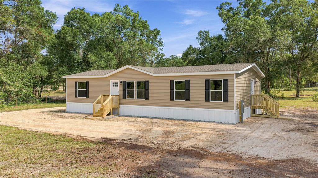 A tan manufactured home with white skirting and wooden stairs sits on a dirt lot — 7314 W EDWARDIAN STREET, DUNNELLON, FL