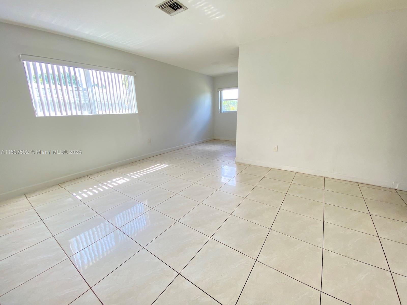 An empty room features white walls, large light-colored floor tiles, and two windows — 1121 NE 214th St, Miami FL 33179, MIAMI, FL
