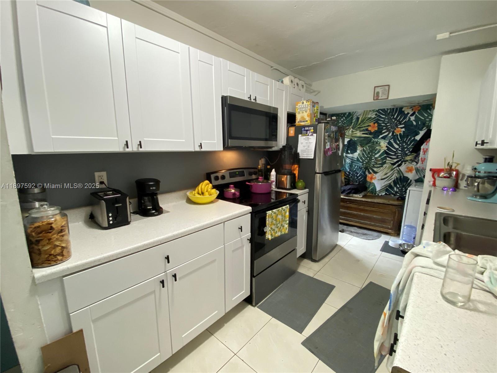 A kitchen features white cabinets, stainless steel appliances, and a tropical-patterned accent wall — 1121 NE 214th St, Miami FL 33179, MIAMI, FL