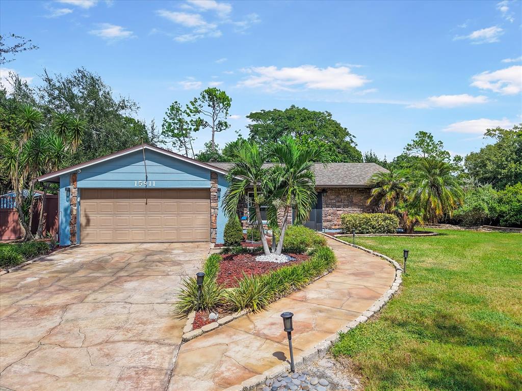 A single-story house with a blue garage, stone facade, and a curved stone walkway — 15911 IRONWARE PLACE, TAMPA, FL