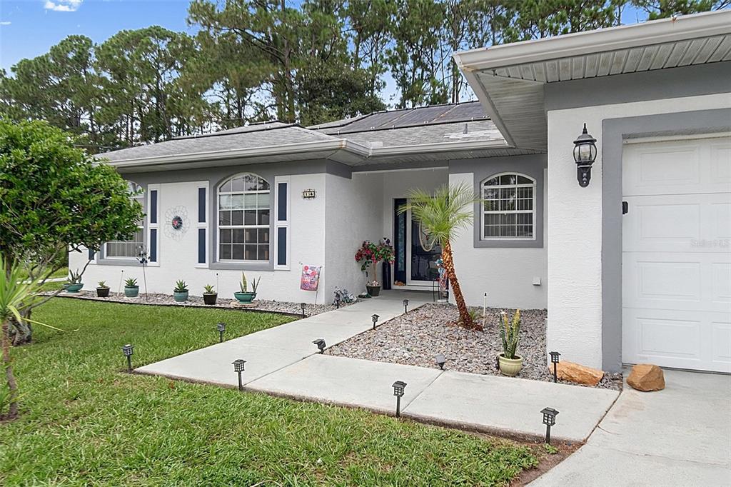 A white single-story house features a gray-trimmed arched window, a front walkway, and landscaping — 14 WILLS PLACE, PALM COAST, FL