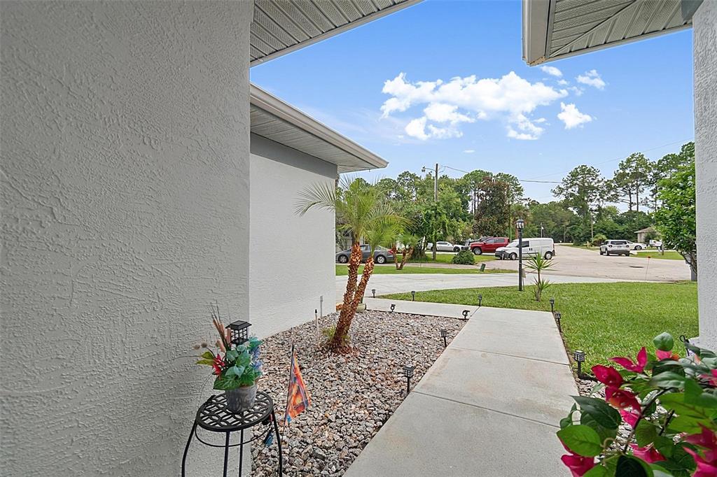 A concrete walkway leads from a covered porch past a small palm tree and landscaping — 14 WILLS PLACE, PALM COAST, FL