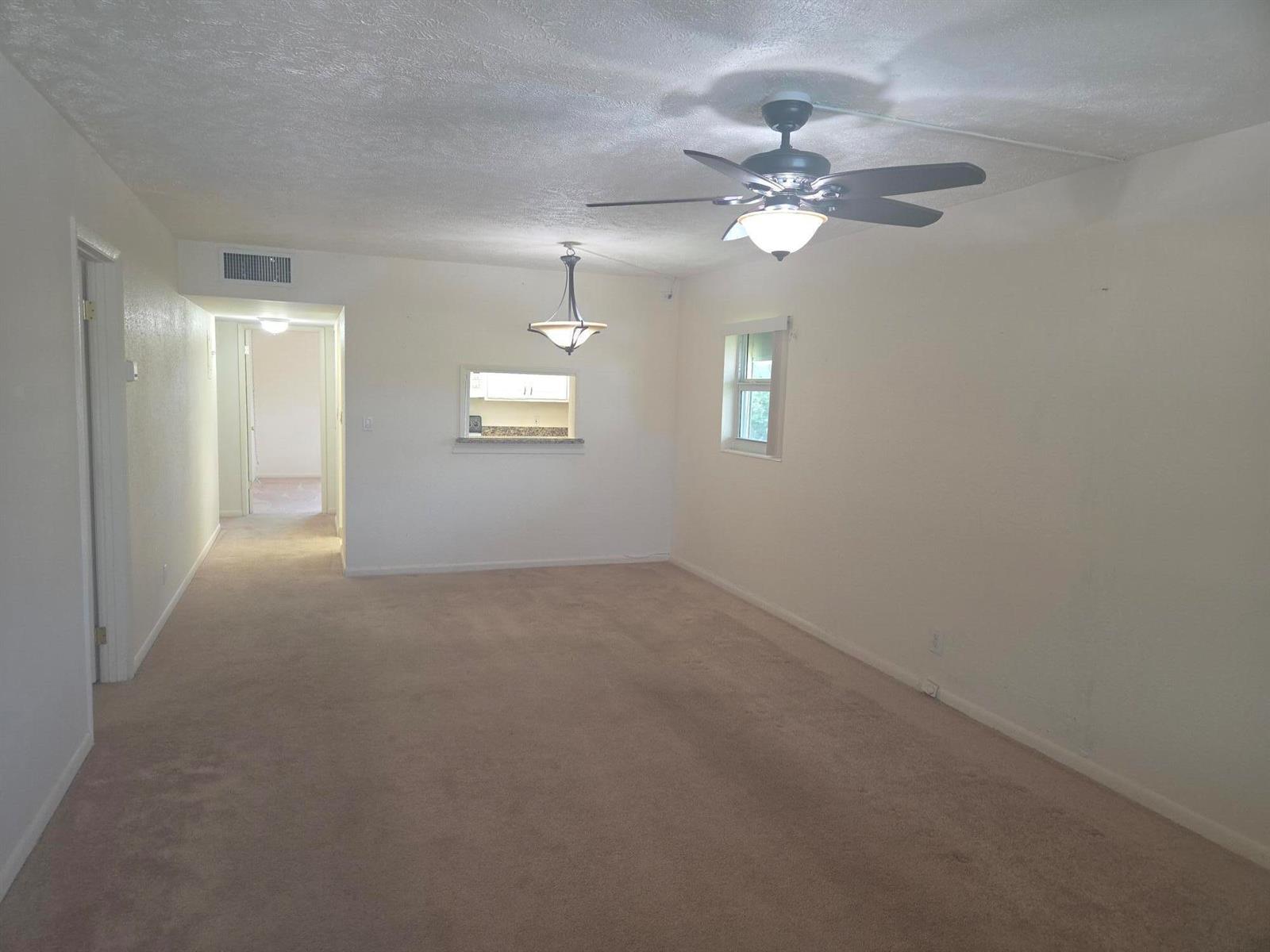 An empty living room with beige carpet, a ceiling fan, and a kitchen pass-through window — 1340 NE 28th Avenue # 228, Pompano Beach FL 33062, POMPANO BEACH, FL