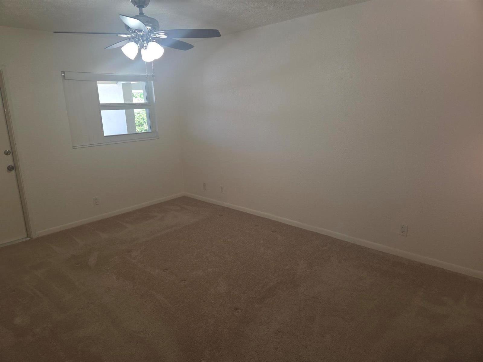 An empty bedroom features beige carpet, white walls, a ceiling fan, and a single window — 1340 NE 28th Avenue # 228, Pompano Beach FL 33062, POMPANO BEACH, FL