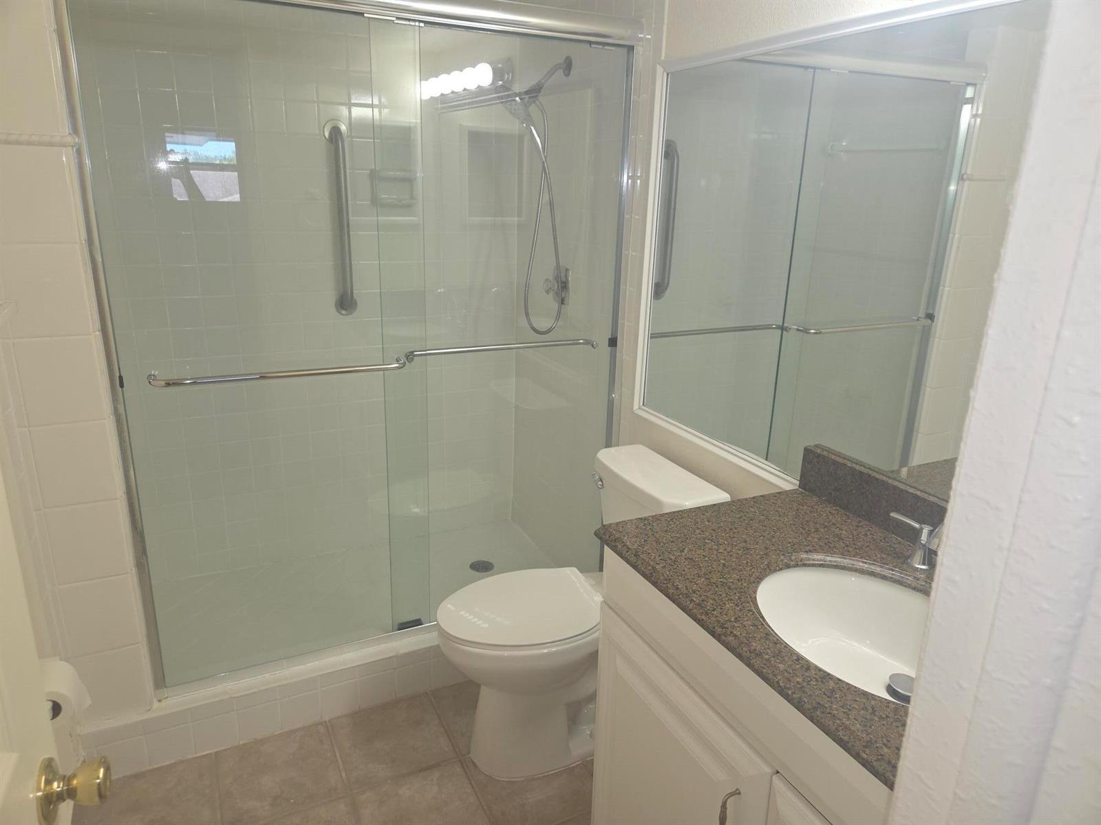 A bathroom features a tiled walk-in shower, a white toilet, and a granite-topped vanity — 1340 NE 28th Avenue # 228, Pompano Beach FL 33062, POMPANO BEACH, FL