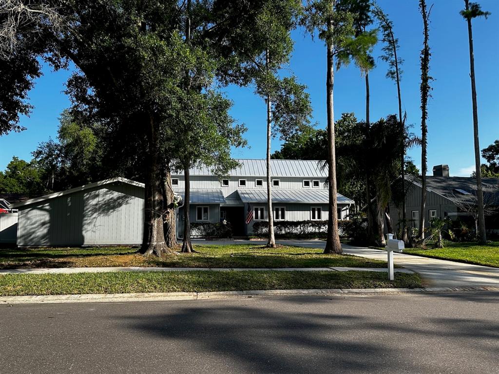 A two-story house with a metal roof and gray siding sits behind trees and grass — 3421 BRIAN ROAD S, PALM HARBOR, FL