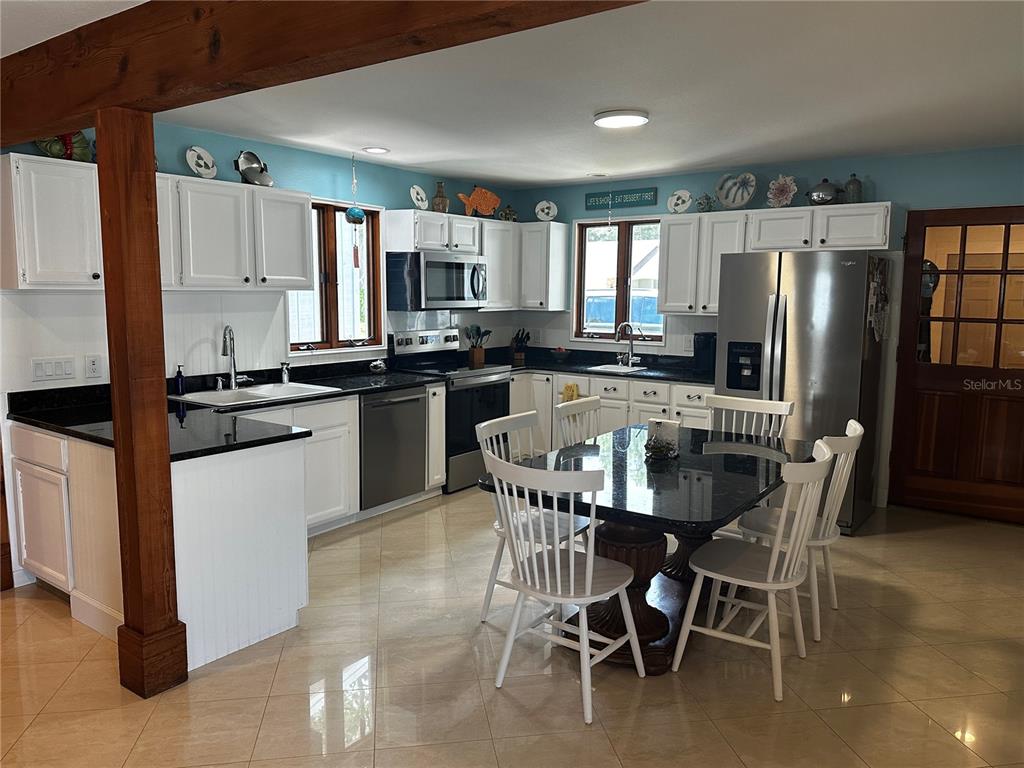 A kitchen features white cabinets, black countertops, stainless steel appliances, and a dining table — 3421 BRIAN ROAD S, PALM HARBOR, FL