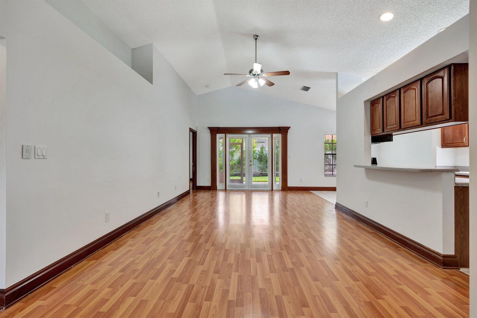 A living room with vaulted ceilings, wood-look flooring, and a kitchen pass-through window — 6149 Foster Street, Jupiter FL 33458, JUPITER, FL