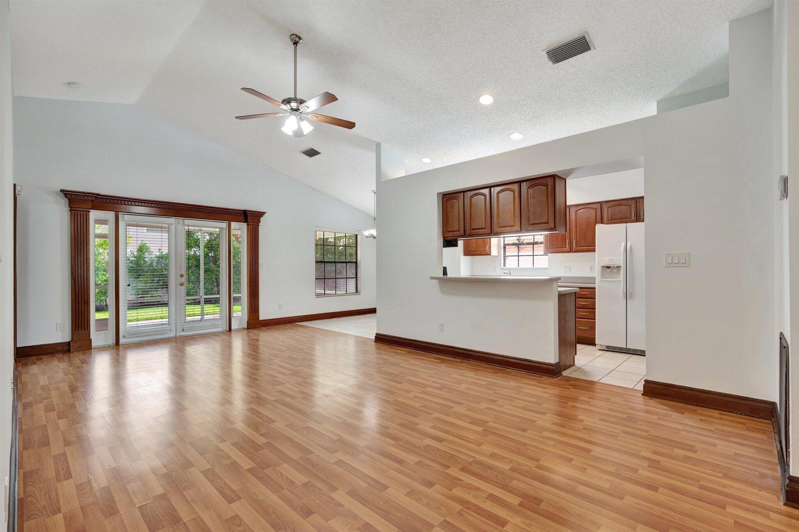 A living room with wood-look flooring, vaulted ceilings, and an open kitchen with wood cabinets — 6149 Foster Street, Jupiter FL 33458, JUPITER, FL