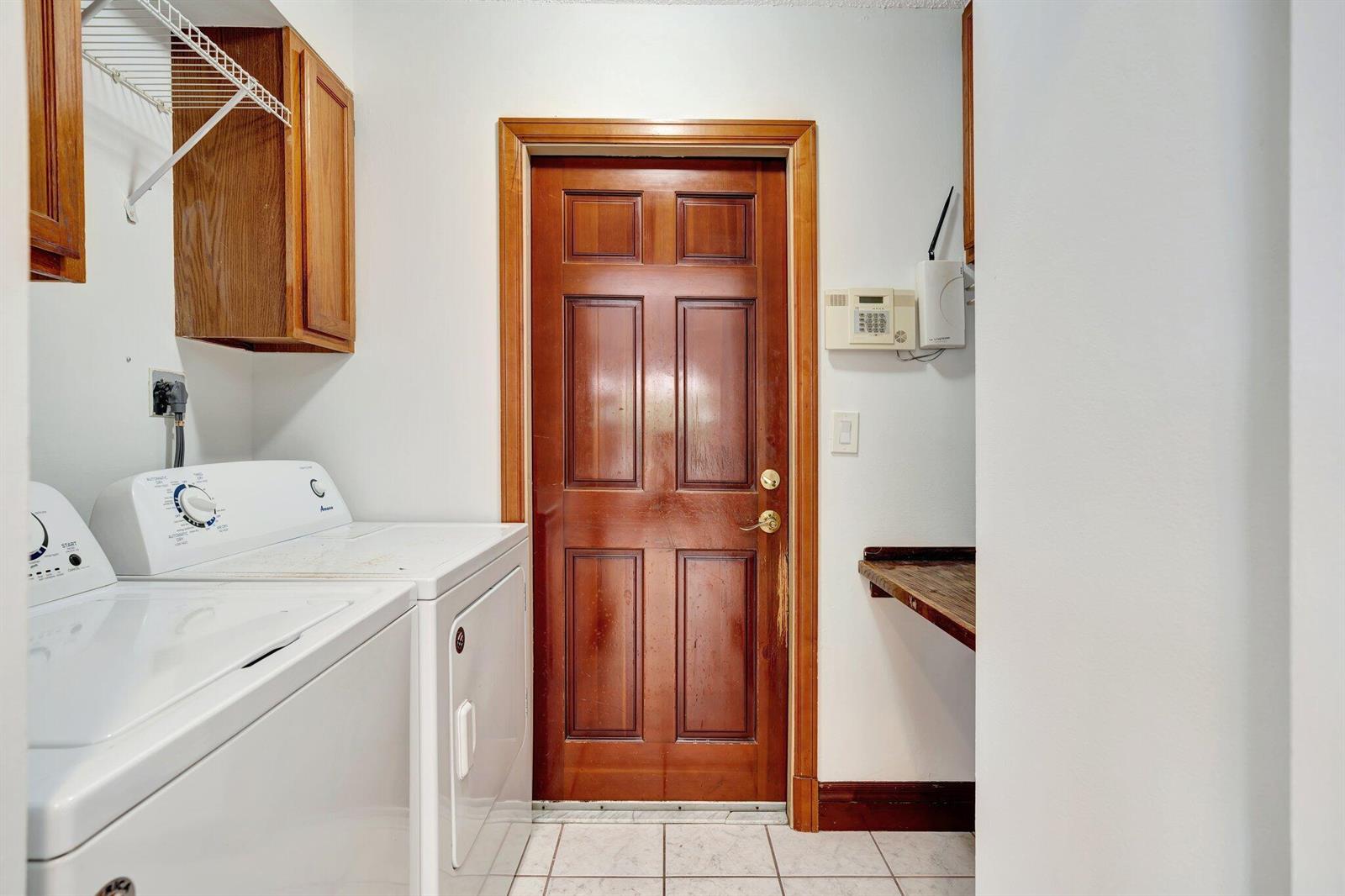 A laundry room features white appliances, wooden cabinets, a wooden door, and tiled flooring — 6149 Foster Street, Jupiter FL 33458, JUPITER, FL