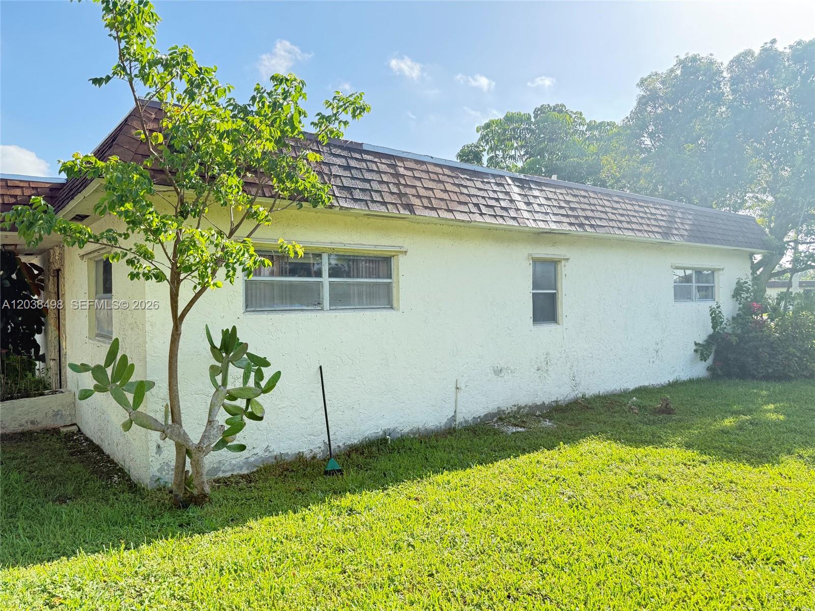 The exterior of a white stucco house features a brown shingled roof and a small tree — 417 SW Natura Ave # A, Deerfield Beach FL 33441, DEERFIELD BEACH, FL