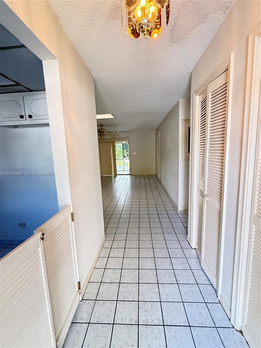 A tiled hallway leads from a foreground entryway toward a living area with sliding doors — 417 SW Natura Ave # A, Deerfield Beach FL 33441, DEERFIELD BEACH, FL