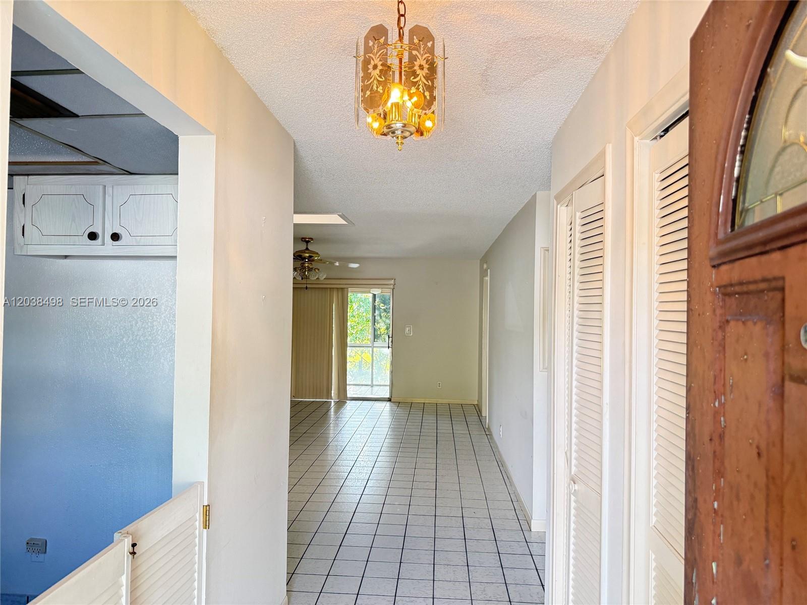 A tiled entryway leads into a living area with a sliding glass door and chandelier — 417 SW Natura Ave # A, Deerfield Beach FL 33441, DEERFIELD BEACH, FL