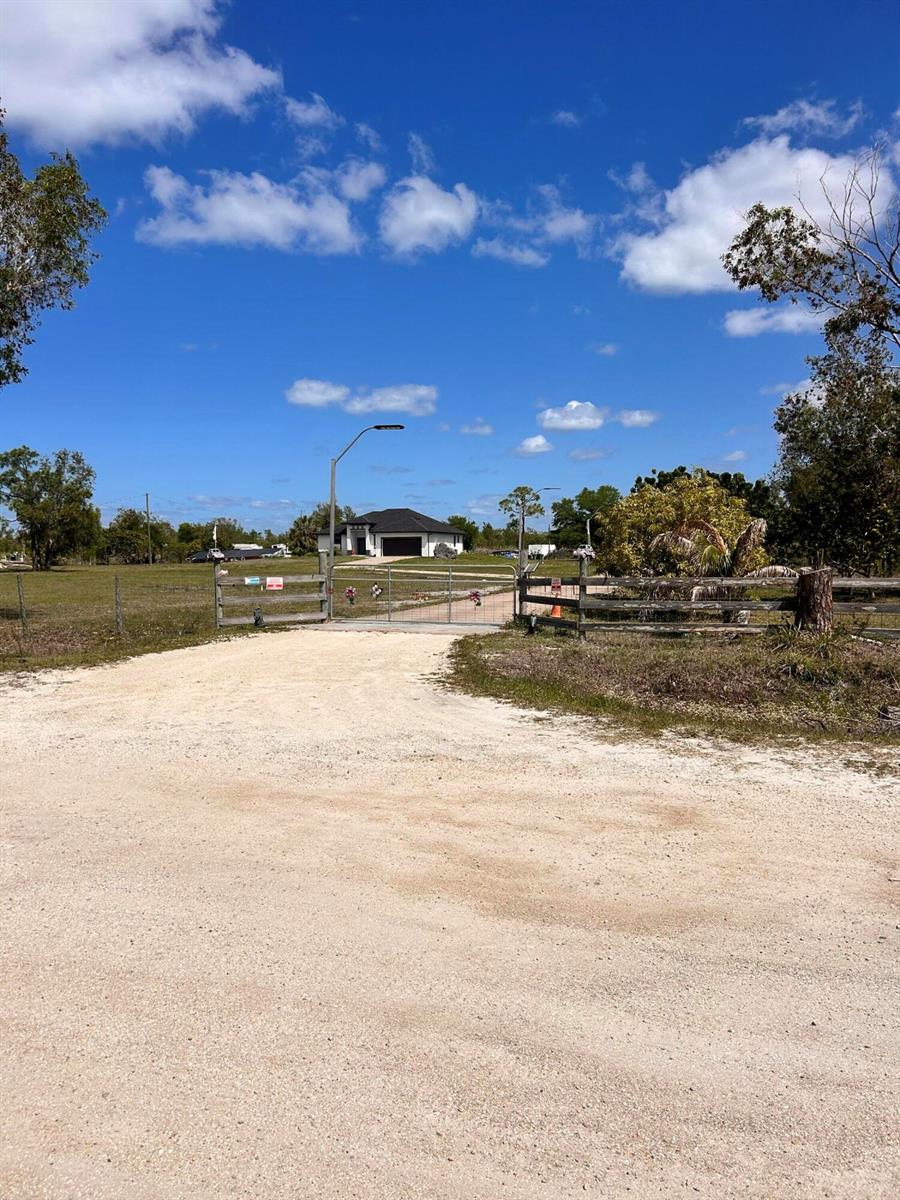 A gravel driveway leads to a gated entrance with a house visible in the distance — 3401 Sand Road, Cape Coral FL 33993, CAPE CORAL, FL