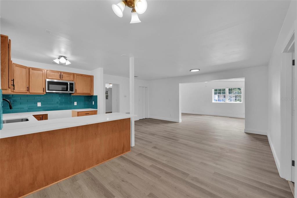 A kitchen with wood cabinets and a teal backsplash opens to a spacious living area — 1110 BUSAC AVENUE, JACKSONVILLE, FL