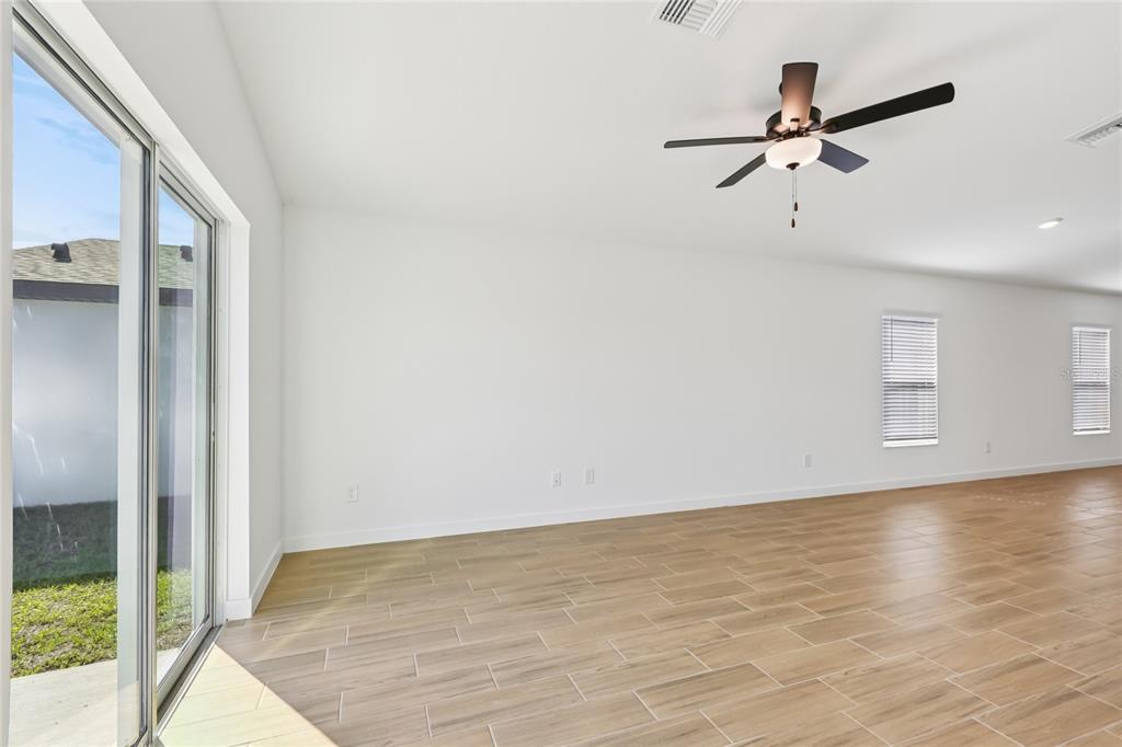 An empty living room with wood-look tile floors, a ceiling fan, and sliding glass doors — 5223 CAP ROAD, BROOKSVILLE, FL