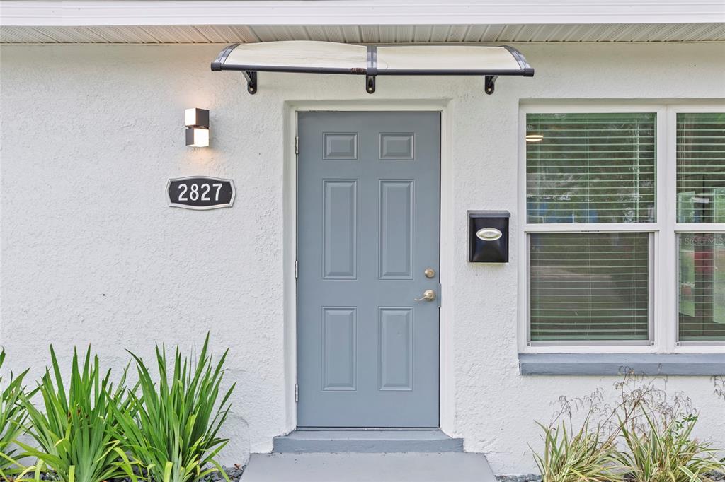 A gray front door with a small awning and house number on a white wall — 2827 16TH AVENUE S, ST PETERSBURG, FL
