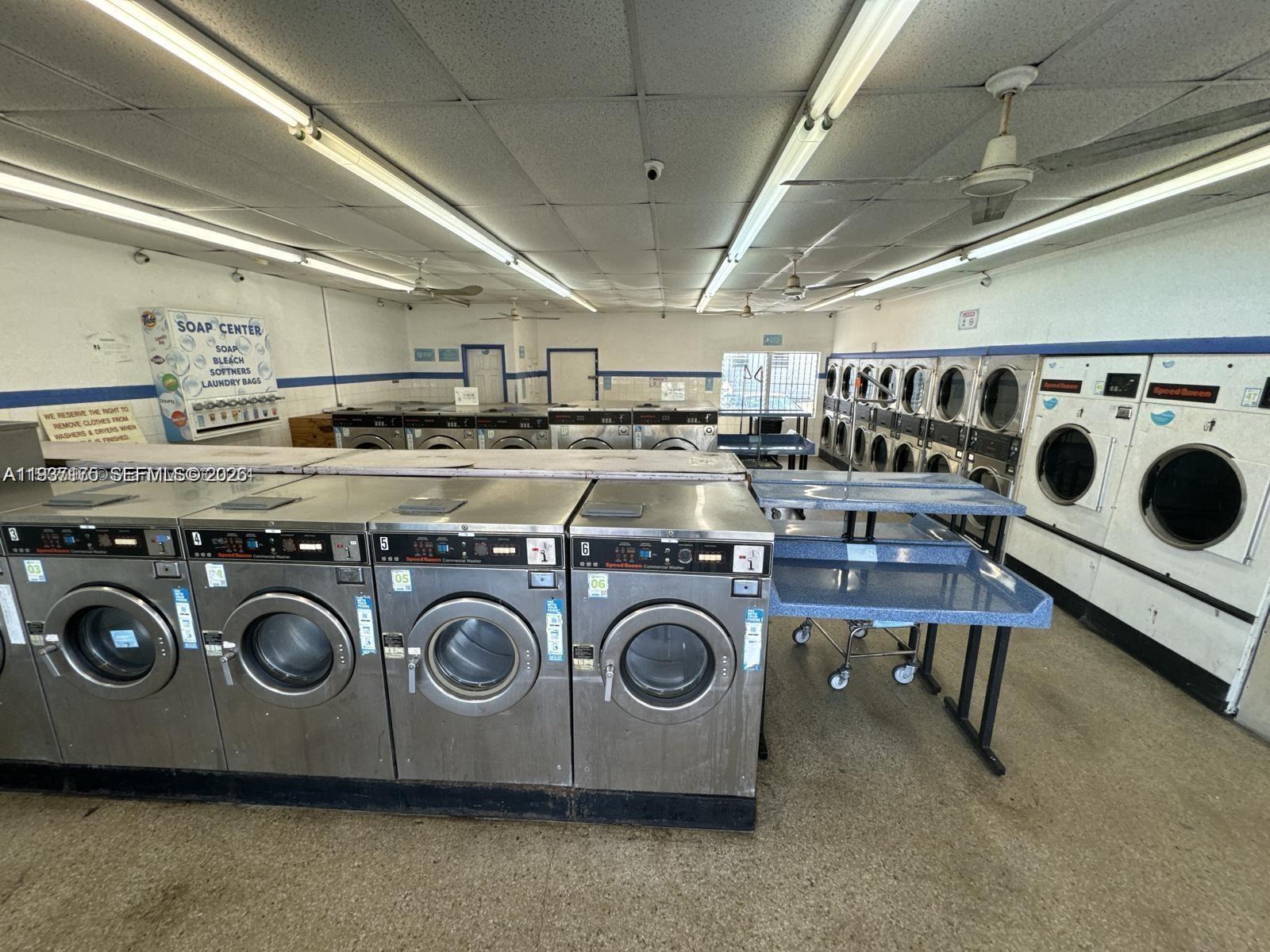 A commercial laundromat features rows of stainless steel washing machines and white dryers — Laundromat Hallandale Beach, Hallandale Beach FL 33009, HALLANDALE BEACH, FL