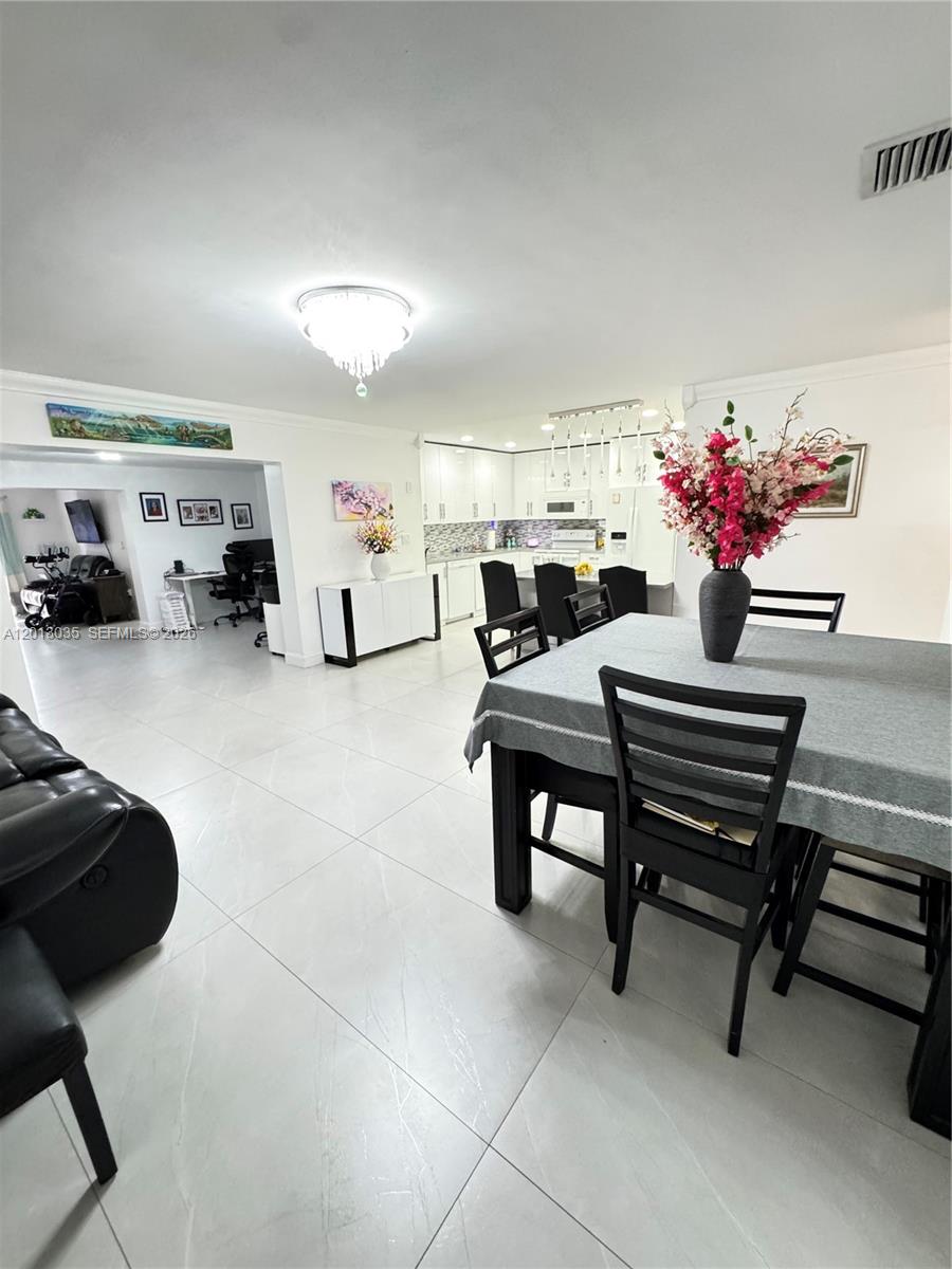 An open-concept dining area and kitchen feature white tile floors and a crystal chandelier — 7140 W 15th Ct, Hialeah FL 33014, HIALEAH, FL
