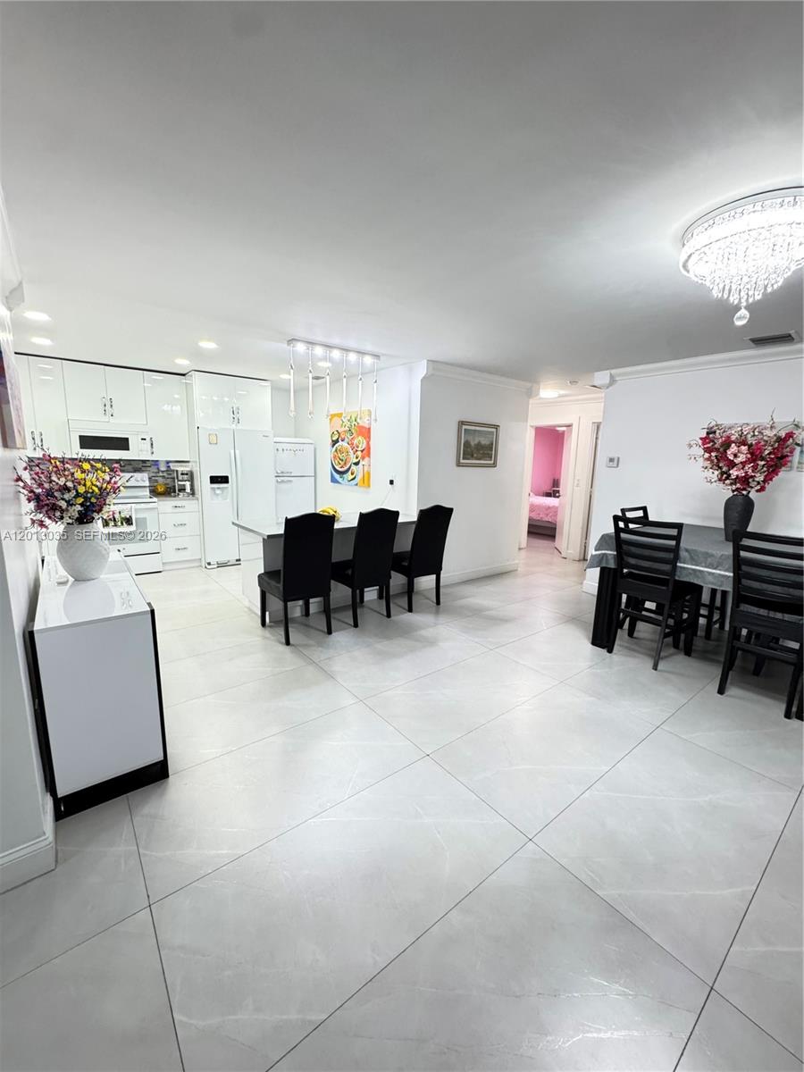 An open-concept kitchen and dining area features white cabinetry, tile flooring, and modern lighting — 7140 W 15th Ct, Hialeah FL 33014, HIALEAH, FL