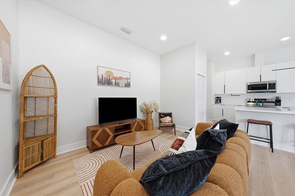 A living room with a brown sofa, television, media console, and an open kitchen — 2644 42ND AVENUE N, ST PETERSBURG, FL