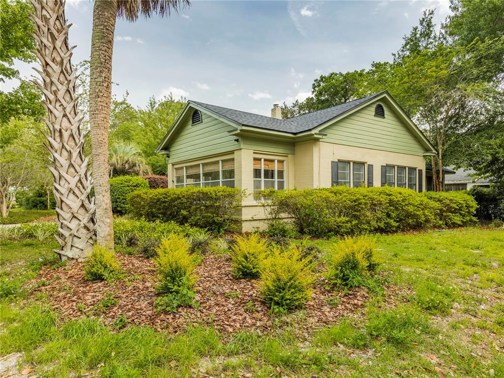 A one-story house with green siding and a tan stucco base sits behind landscaped bushes — 501 NE 8TH AVENUE, GAINESVILLE, FL