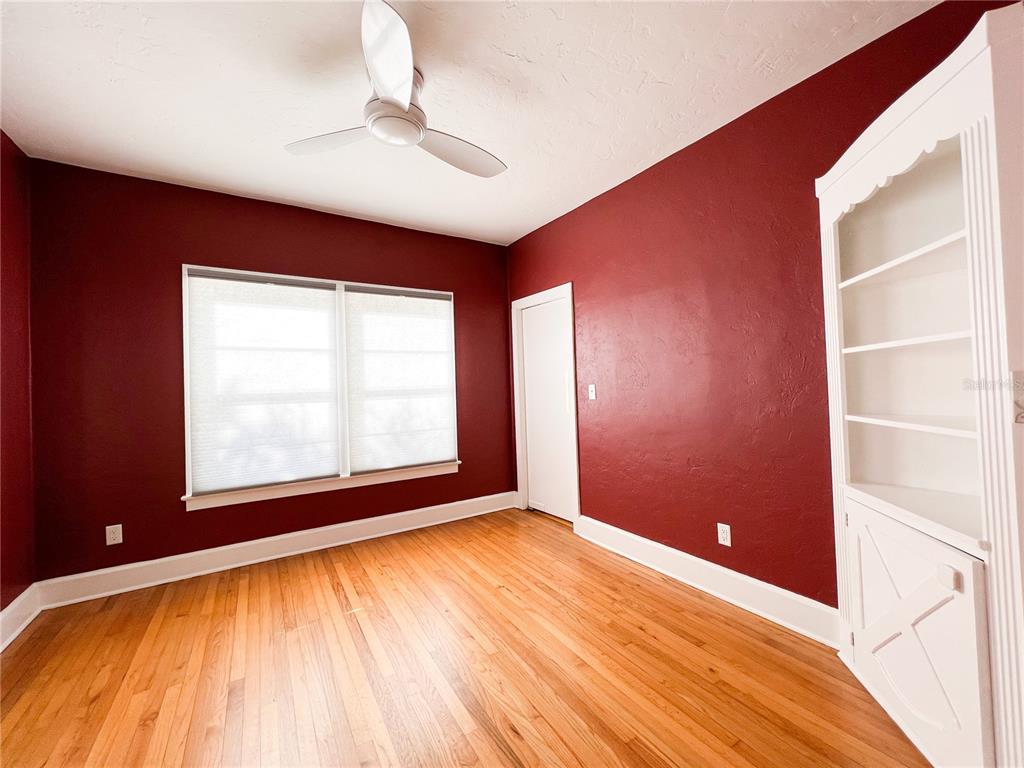 An empty room with red walls, hardwood floors, a ceiling fan, and a white bookshelf — 501 NE 8TH AVENUE, GAINESVILLE, FL