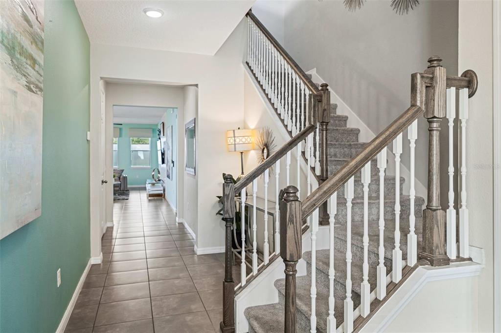 A tiled entryway features a carpeted staircase with wooden railings and a view into a room — 9079 SUNSHINE RIDGE LOOP, KISSIMMEE, FL
